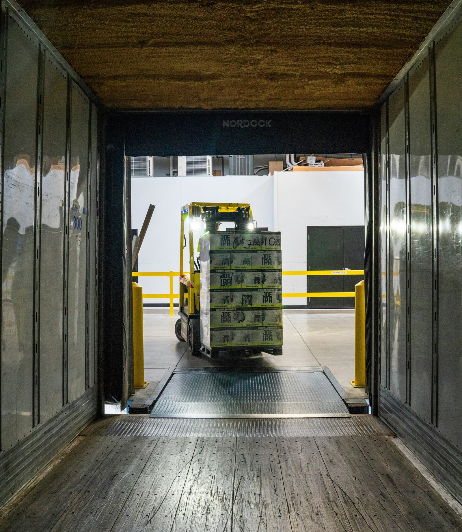 Warehouse worker scanning a large red product box while holding another parcel in a well-organised fulfilment centre.